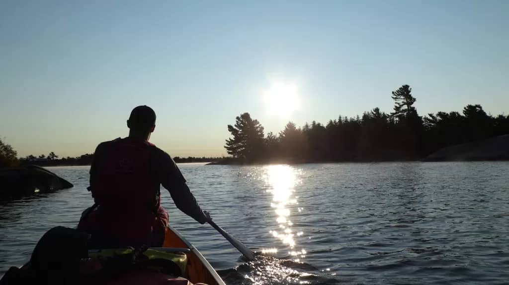 picture of a man paddling a canoe toward trees while the sun is setting in the backcountry of Ontario Provincial Parks