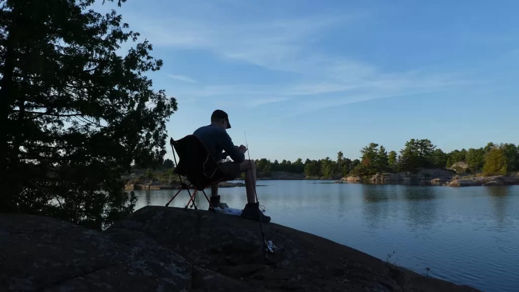 picture of a man in sillouette against a lake while backcountry camping in an Ontario Provincial Park with a fishing rod