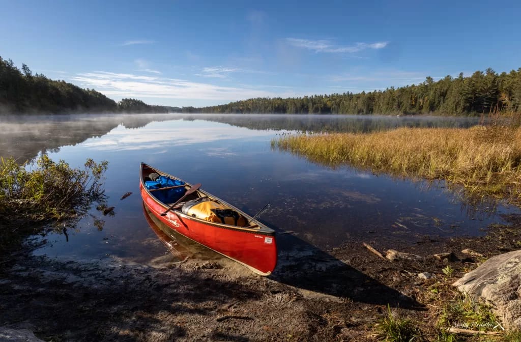 picture of a red canoe backcountry camping with a beautiful lake and blue sky