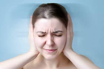 woman with tinnitus holding her ears to make the ringing stop or get rid of tinnitus