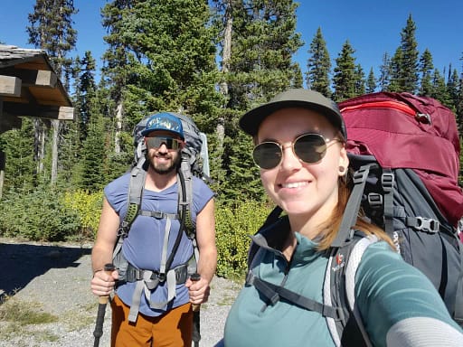 picture of a woman and a man wearing backpacks who are about to hike the Assiniboine trail in Canada